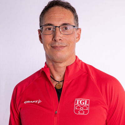 Eine lächelnder Mann trägt eine rote TGL-Jacke, symbolisierend den Sportgeist des Vereins Turngemeinde Landshut.