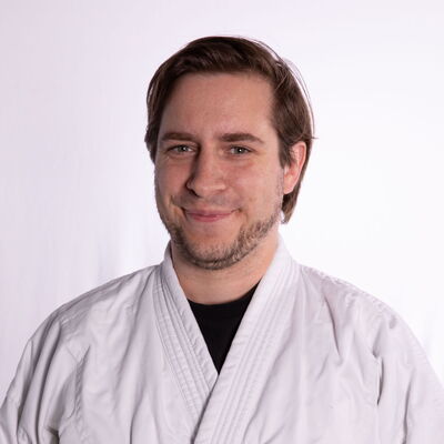 Eine Frau in einem weißen Judoanzug mit dem Logo der Turngemeinde Landshut lächelt in die Kamera.