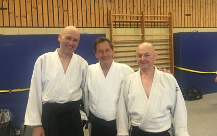 Drei Männer in weißen Kampfsportanzügen lächeln in einer Turnhalle der Turngemeinde Landshut.