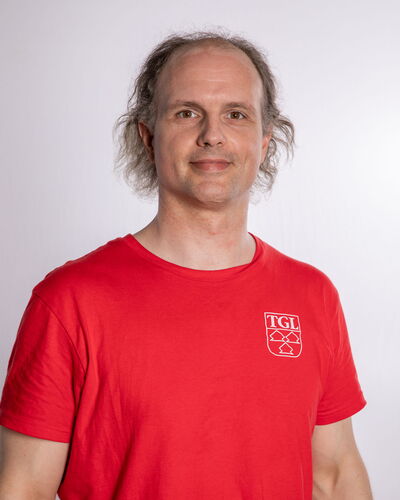 Ein Mann in einem roten TGL-Shirt der Turngemeinde Landshut lächelt vor einem neutralen Hintergrund.