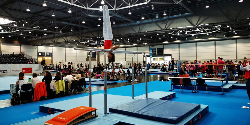 Ein Turner der Turngemeinde zeigt eine beeindruckende Übung am Barren bei einem Wettkampf in einer großen Sporthalle.