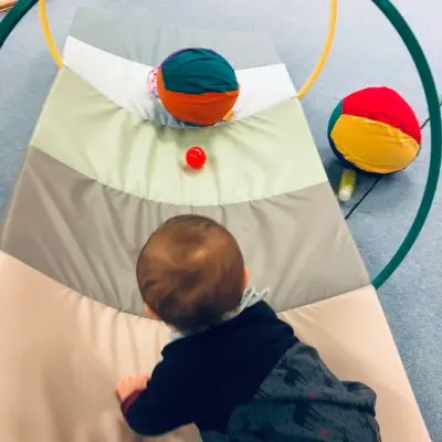 Ein Baby krabbelt in einem Sportkurs der Turngemeinde über eine weiche Matte zu bunten Bällen.