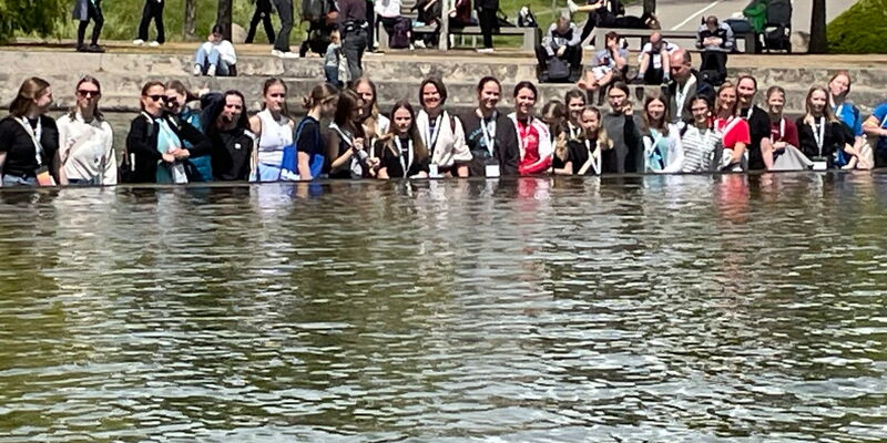 Eine Gruppe von Menschen steht am Wasser und genießt gemeinsam einen sonnigen Tag, passend zum Motto der Turngemeinde.