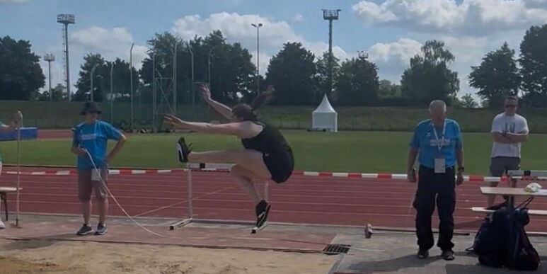 Eine Athletin der Turngemeinde beim Weitsprung in Landshut, beobachtet von Kampfrichtern am Sandbecken.