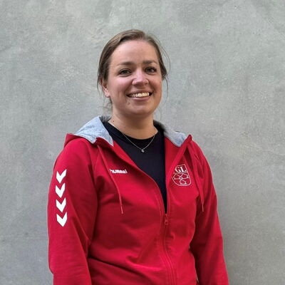 Eine Frau in einem roten TGL-Shirt der Turngemeinde Landshut lächelt vor einem neutralen Hintergrund.