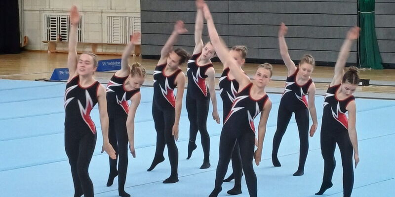 Ein Team der Turngemeinde Landshut führt eine synchronisierte Gymnastikroutine auf blauen Matten auf.