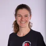 Eine Frau lächelt in die Kamera und trägt ein T-Shirt mit dem Logo des Sportvereins Turngemeinde Landshut.