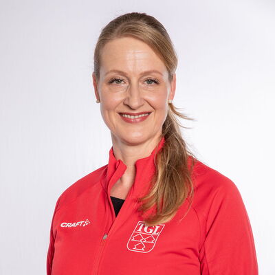 Eine lächelnde Frau trägt eine rote TGL-Jacke, symbolisierend den Sportgeist des Vereins Turngemeinde Landshut.