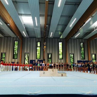 Turnerinnen und Turner der Turngemeinde Landshut stehen bei der Vereinsmeisterschaft in einer Halle neben einem Podest.