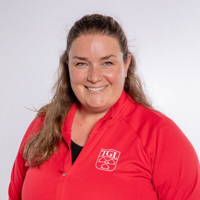 Eine lächelnde Frau trägt eine rote TGL-Jacke, symbolisierend den Sportgeist des Vereins Turngemeinde Landshut.