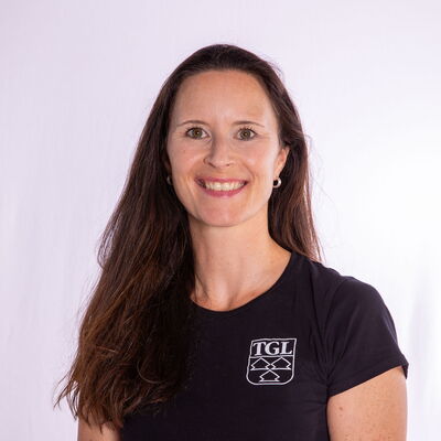 Eine Frau im schwarzen T-Shirt mit TGL-Logo lächelt freundlich in die Kamera, repräsentiert den Sportverein.