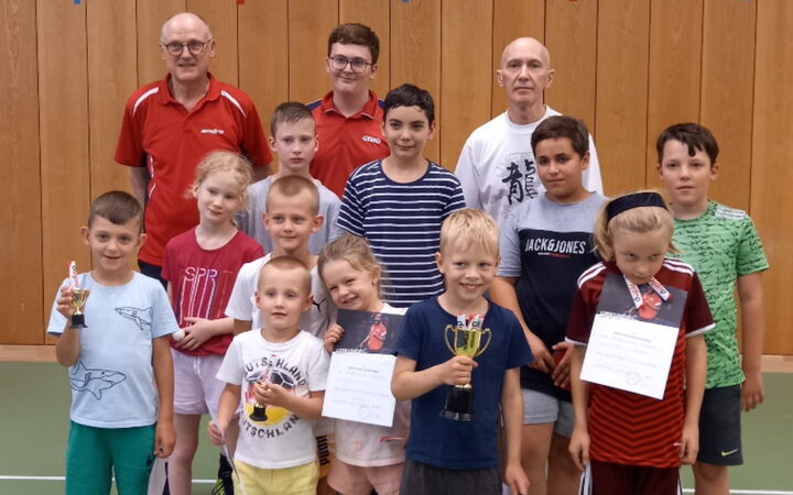 Eine Gruppe von Kindern und Erwachsenen hält Pokale und Urkunden bei einer Tischtennisveranstaltung des Vereins Turngemeinde Landshut.