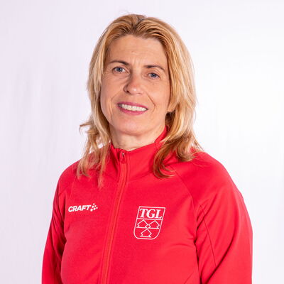 Eine lächelnde Frau trägt eine rote TGL-Jacke, symbolisierend den Sportgeist des Vereins Turngemeinde Landshut.