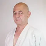 Ein lächelnder Mann in einem weißen Aikidoanzug, aufgenommen in einer Sporthalle, repräsentiert den Verein Turngemeinde.