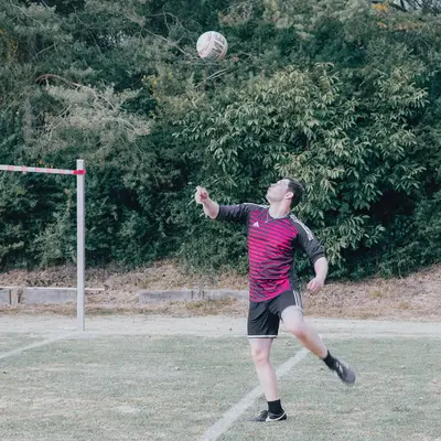 Ein Sportler der Turngemeinde springt auf dem Feld, um einen Ball zu schlagen, mit Bäumen im Hintergrund.