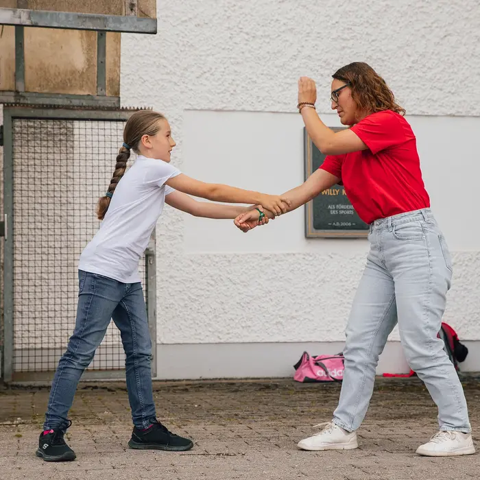 Ein Mädchen und eine Frau üben Selbstverteidigungstechniken bei einem Turngemeinde-Kurs im Freien.