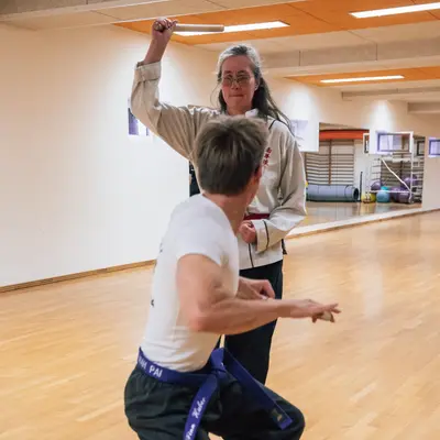 Zwei Personen üben Kampftechniken mit Stöcken in einer Turnhalle der Turngemeinde Landshut.
