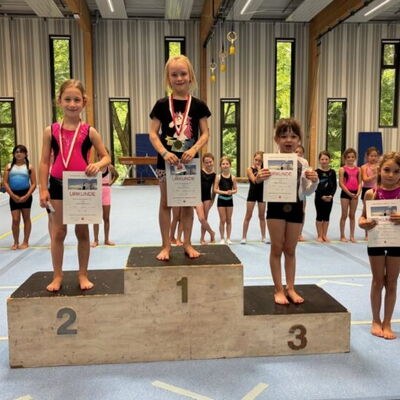 Drei junge Turnerinnen stehen auf dem Siegerpodest und präsentieren stolz ihre Urkunden bei einem Turngemeinde-Wettbewerb.