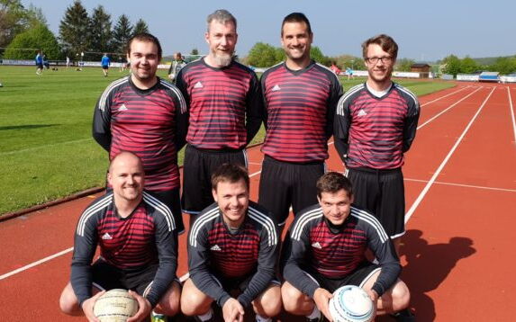 Eine Sportmannschaft der Turngemeinde Landshut posiert lachend in ihren Vereins-Trikots auf einer Laufbahn.