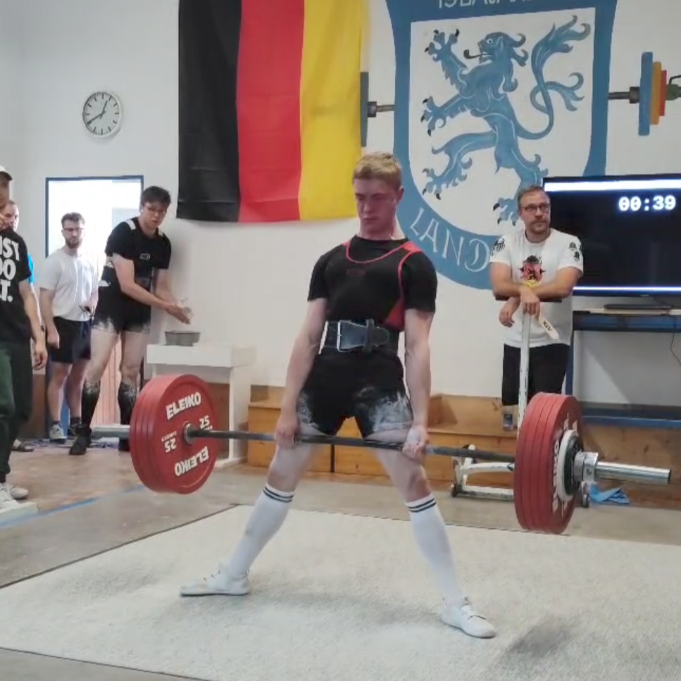 Ein Gewichtheber hebt eine Langhantel bei einem Wettkampf der Turngemeinde Landshut, während Zuschauer applaudieren.