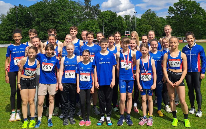 Eine Gruppe von jungen Leichtathleten des Vereins Turngemeinde Landshut posiert lächelnd für ein Foto auf dem Sportplatz.