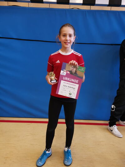 Ein Mädchen hält stolz eine Urkunde und einen Pokal in der Turnhalle des Sportvereins Turngemeinde Landshut.