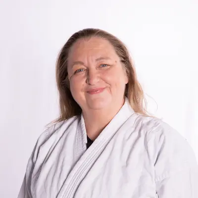 Eine Frau in einem weißen Gi lächelt freundlich in die Kamera, was den Teamgeist der Turngemeinde Landshut widerspiegelt.