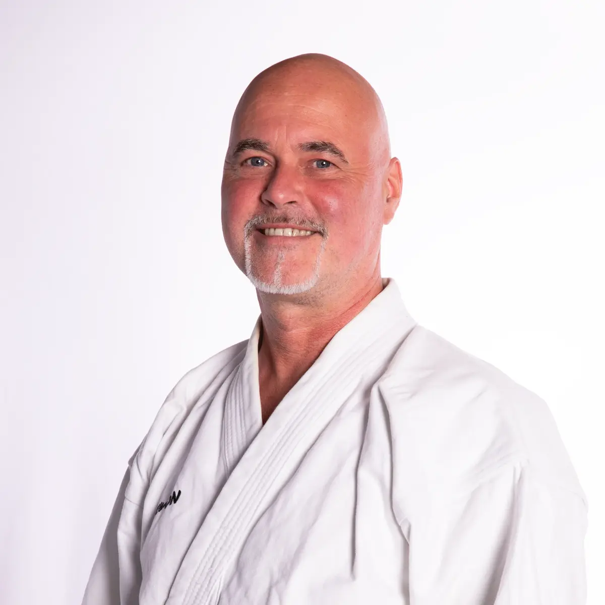 Ein Mann in einem weißen Kampfsportanzug lächelt freundlich in die Kamera, repräsentierend den Sportverein Turngemeinde Landshut.