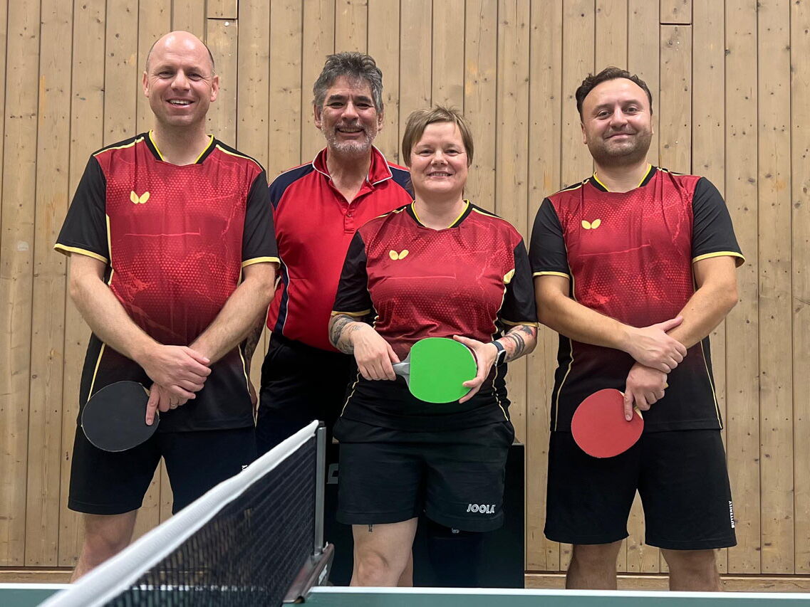 Vier Personen im einheitlichen Sporttrikot posieren in einer Sporthalle der Turngemeinde Landshut für ein Teamfoto.