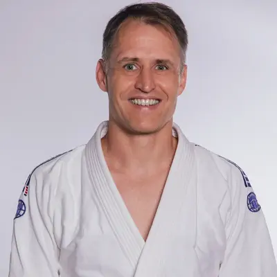 Ein Mann in einem weißen Judo-Gi lächelt freundlich, repräsentiert die Turngemeinde Landshut im Sportverein.