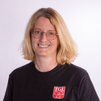 Eine Frau in einem TGL-T-Shirt lächelt freundlich in die Kamera und repräsentiert den Sportverein Turngemeinde Landshut.