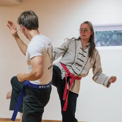 Zwei Personen üben Kampfsport in einem Raum der Turngemeinde Landshut, wobei eine Frau einen Tritt ausführt.