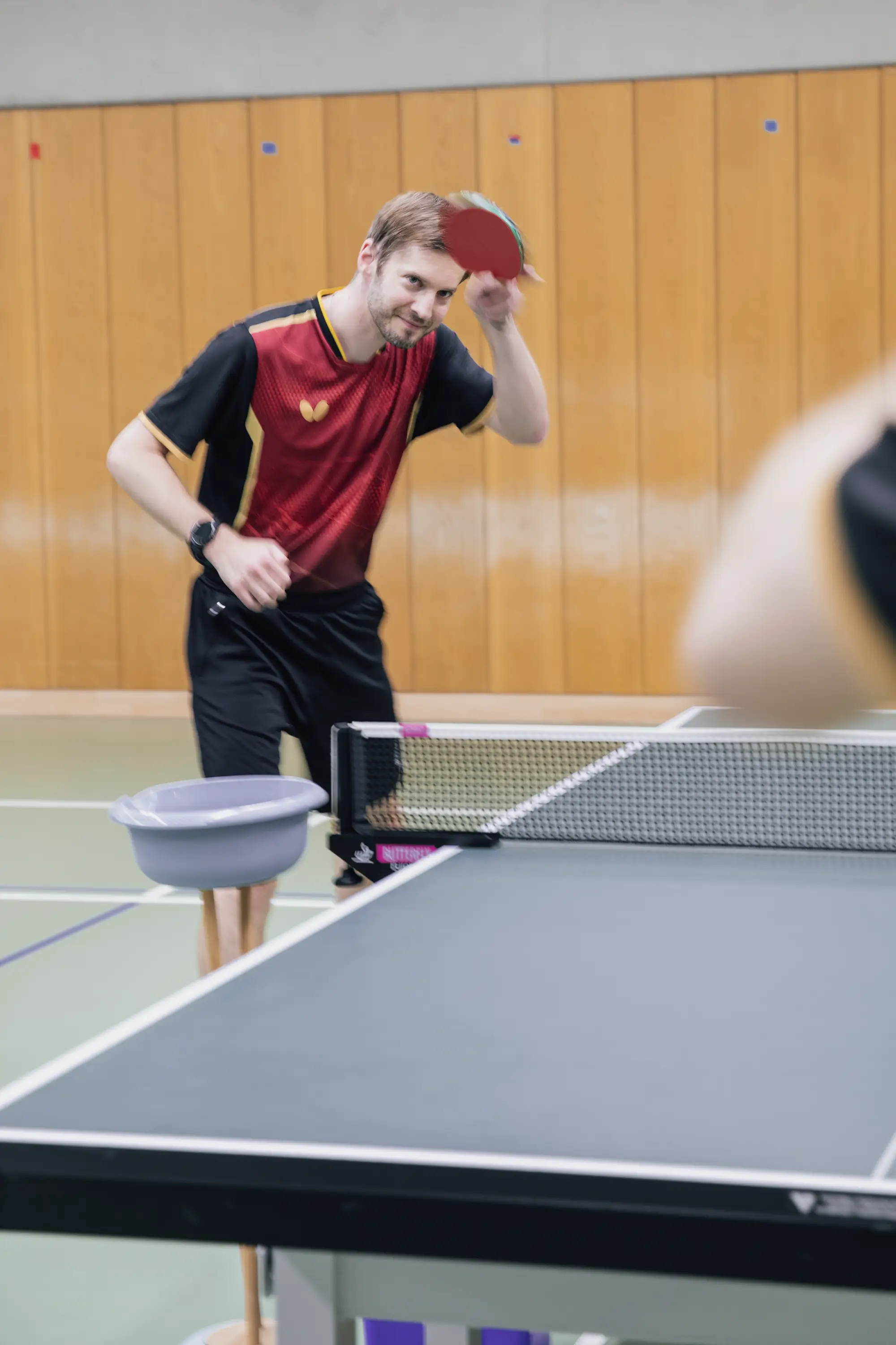Ein Mann im roten Trikot spielt Tischtennis in der Turnhalle von Landshut und repräsentiert den Sportverein TGL.