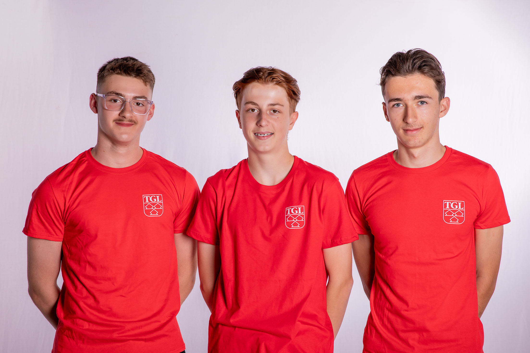 Drei junge Männer in roten TGL-Shirts lächeln und repräsentieren den Sportverein Turngemeinde Landshut.