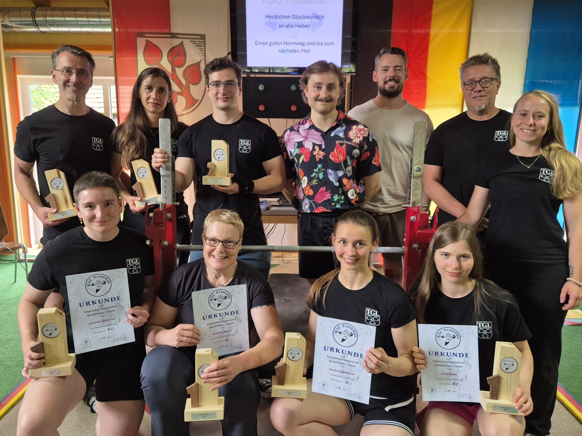 Mitglieder der Turngemeinde Landshut feiern ihren Erfolg bei der Bayerischen Meisterschaft im Bankdrücken mit Urkunden.