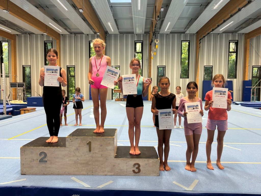 Sechs junge Turnerinnen der Turngemeinde Landshut präsentieren stolz ihre Urkunden nach einem erfolgreichen Wettkampf.
