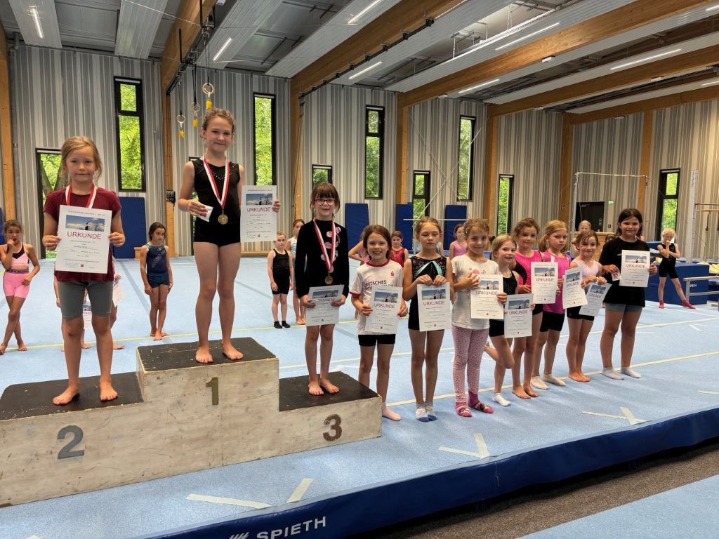 Bei der Turngemeinde Landshut stehen junge Turnerinnen stolz mit Urkunden und Medaillen auf dem Siegerpodest.