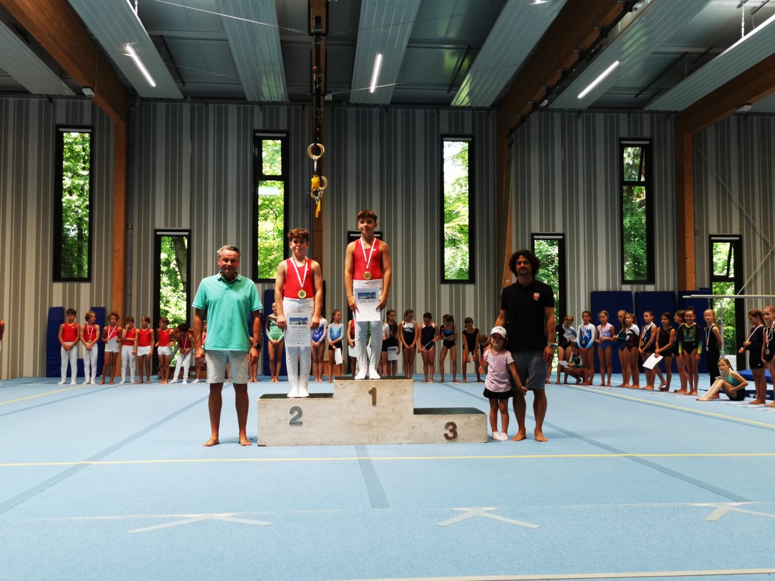 Junge Turner der Turngemeinde Landshut stehen bei einer Siegerehrung auf dem Podest in einer Sporthalle.