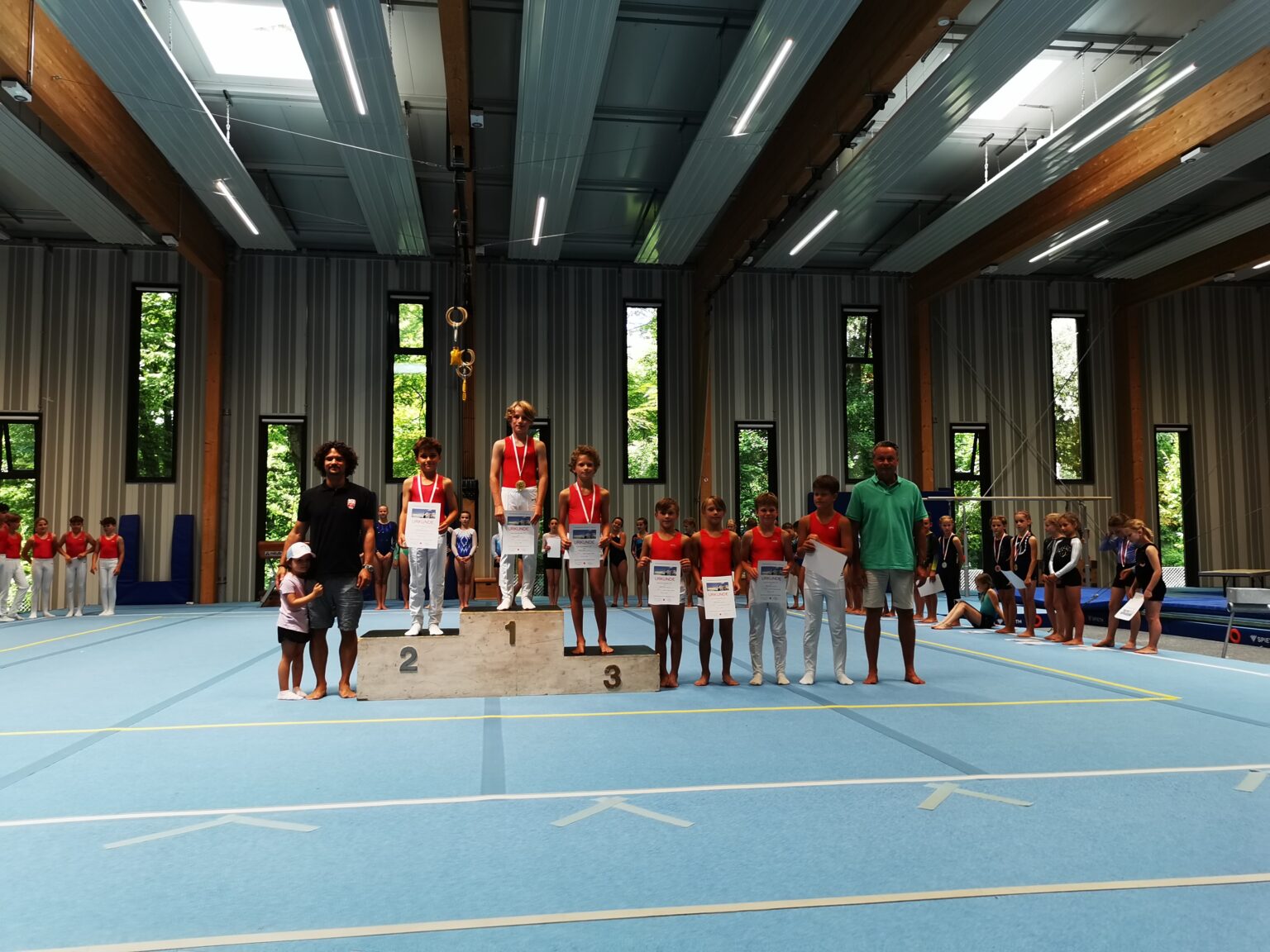 In einer Sporthalle stehen Jungen der Turngemeinde Landshut stolz auf dem Siegerpodest mit Medaillen und Urkunden.
