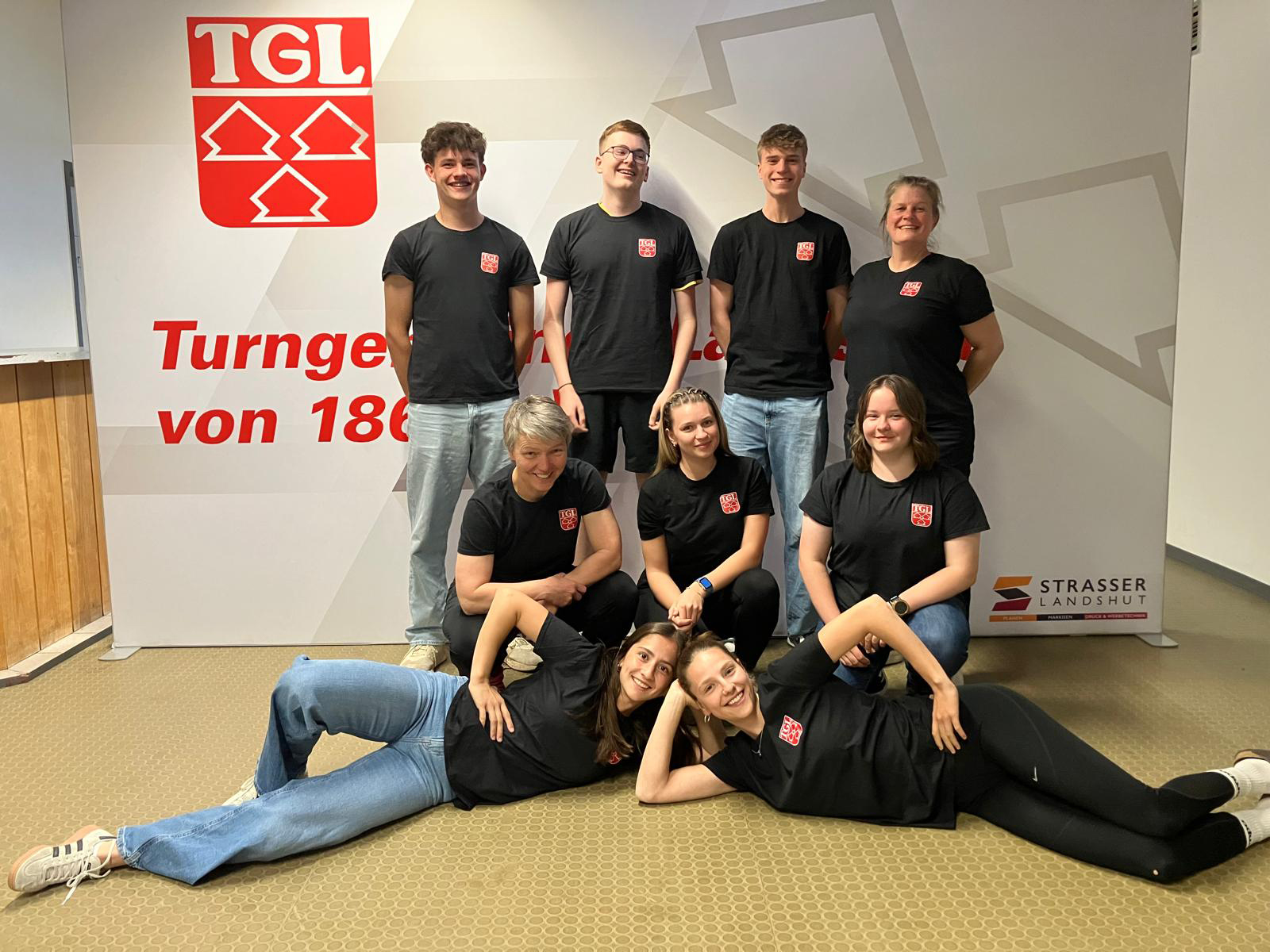 Eine Gruppe Jugendsprecher der Turngemeinde Landshut posiert fröhlich vor einem TGL-Banner.