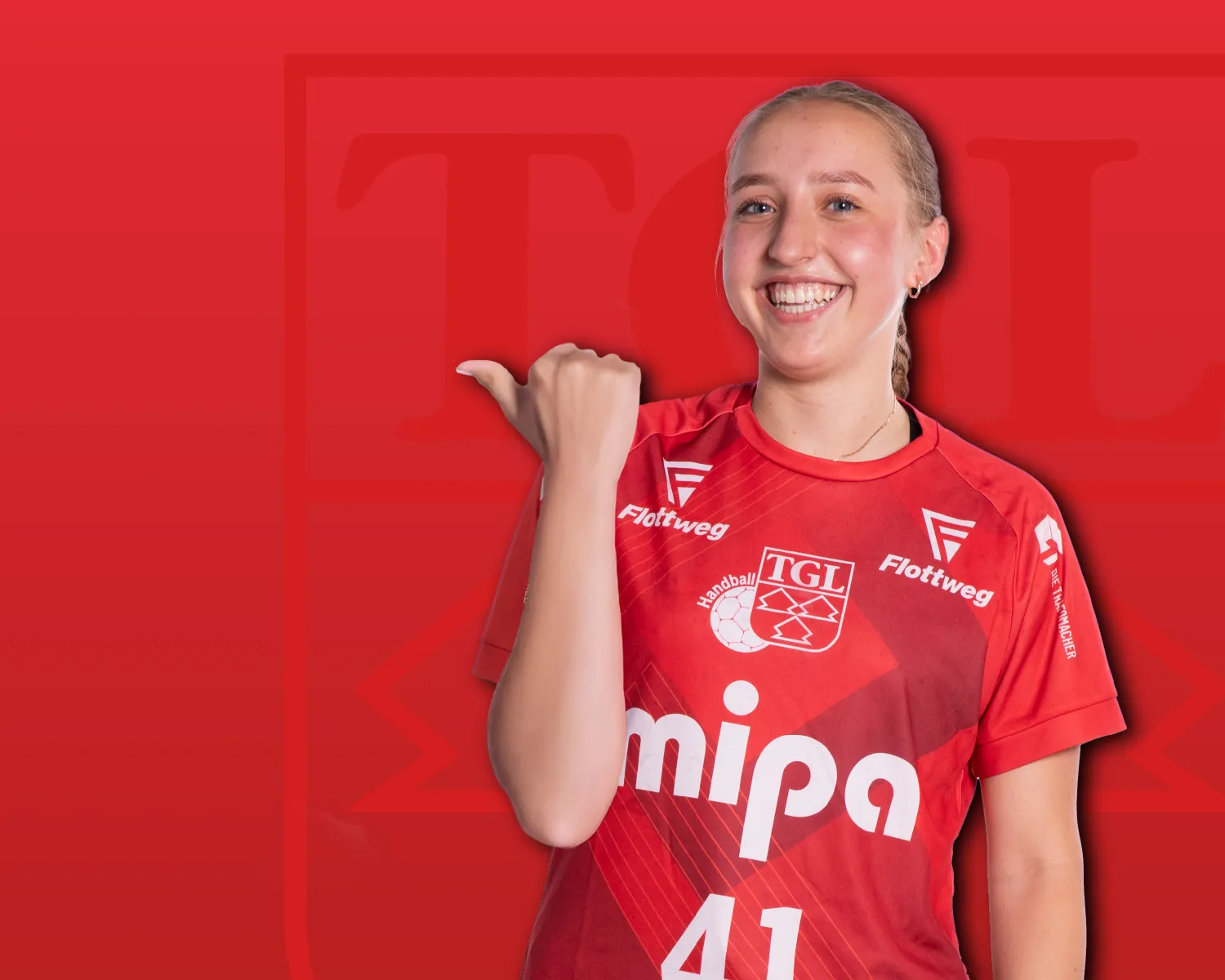 Eine lächelnde Sportlerin im roten TGL-Trikot zeigt auf das Vereinslogo der Turngemeinde Landshut.